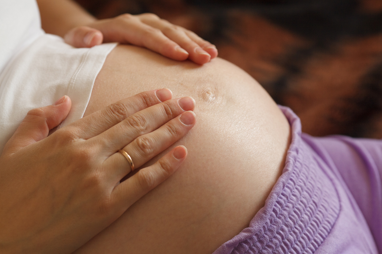 Young pregnant woman holding and touching her belly, closeup